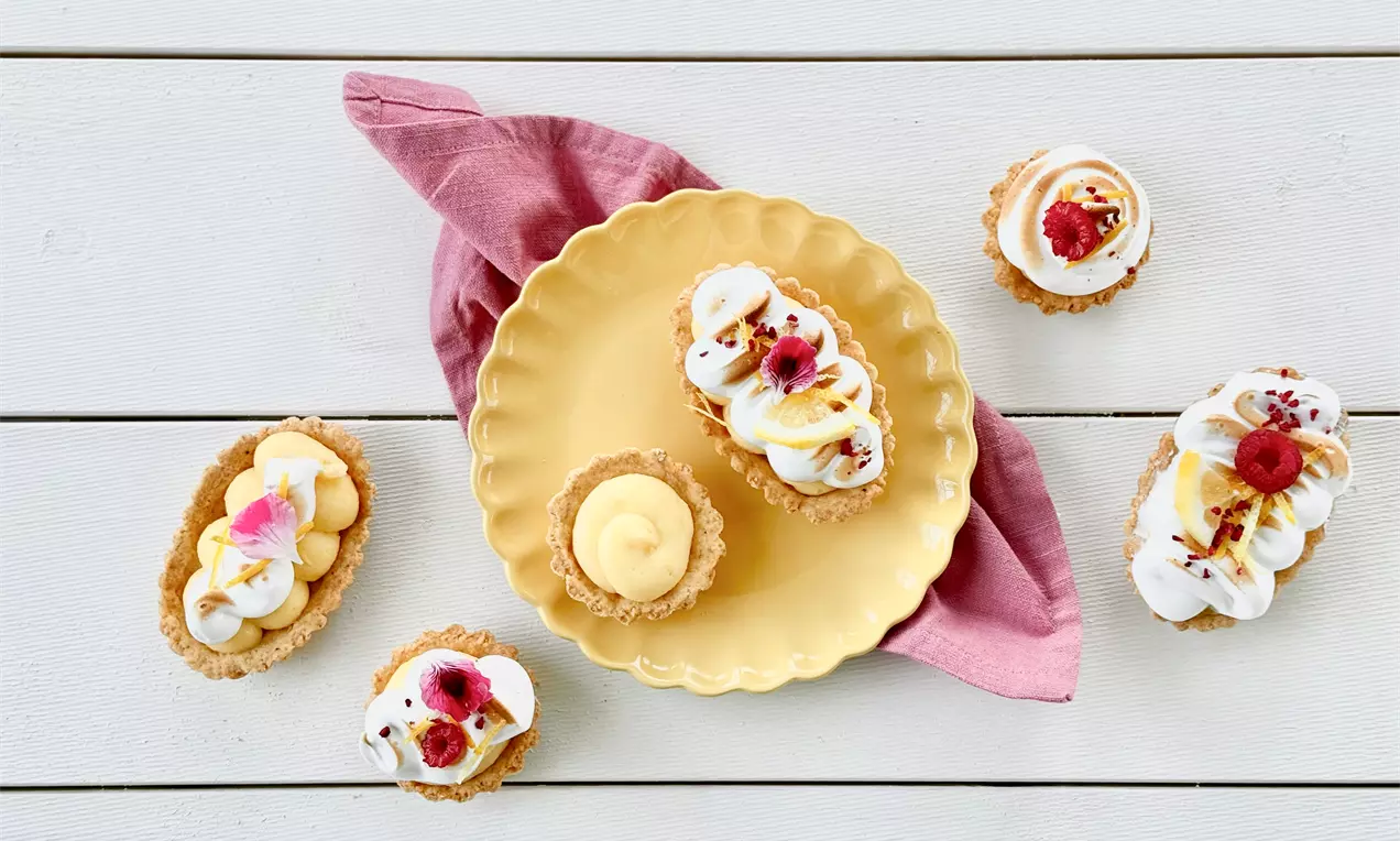 Sitruuna-marenkipiiraat rapeilla korimaisilla pohjilla, ilmavaa valkoista marenkia ja vaaleankeltaista täytettä, koristeltu marjoilla ja kukilla