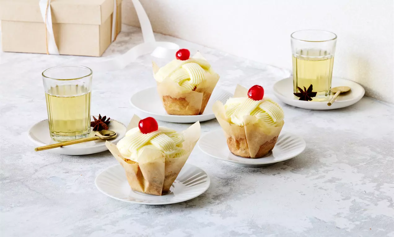 Pehmeitä vaaleita muffinsseja, päällystetty kevyellä kermavaahdolla ja kirkkaanpunaisella kirsikalla, aseteltuna valkoisille lautasille.