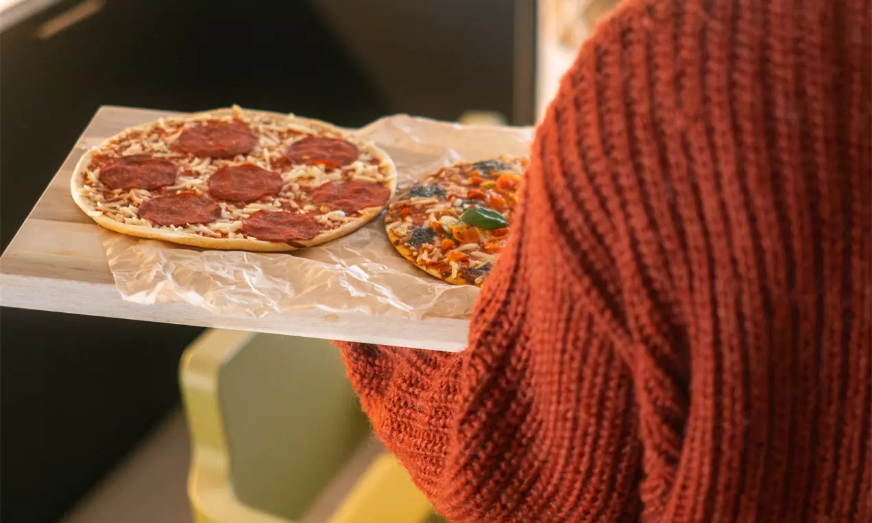 Ohutpohjaiset pizzat lämpimän vaalealla alustalla, toinen täynnä punaisia pepperoniviipaleita, toinen täplikkäänä värikkäitä kasviksia