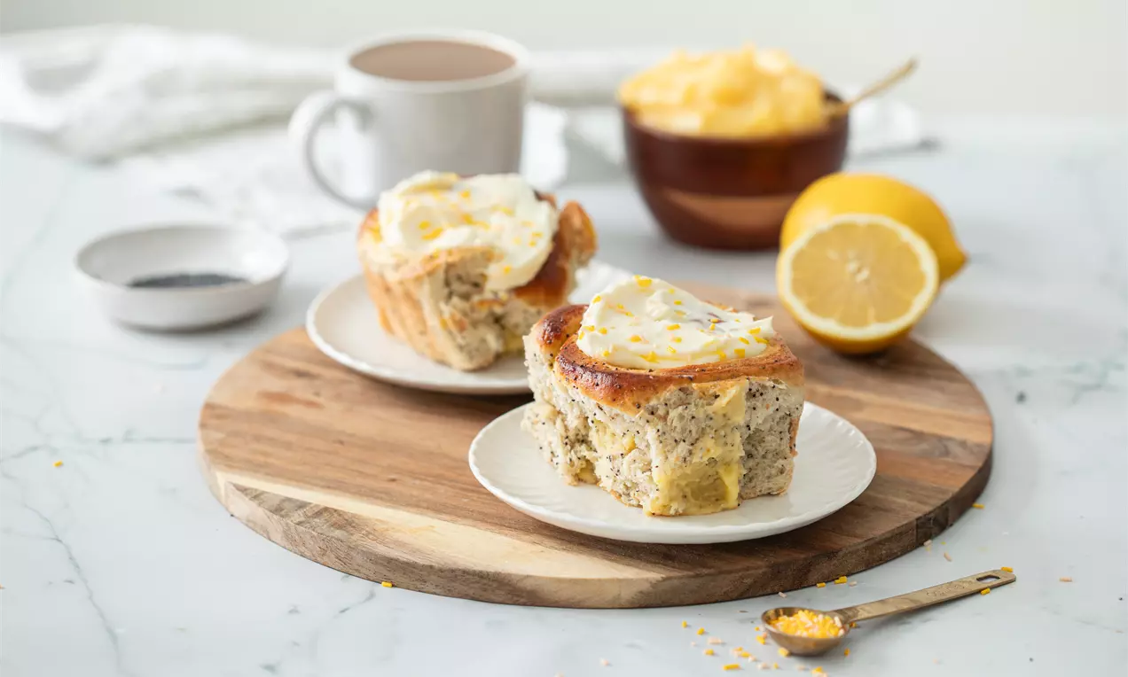 Vaaleankultainen sitruunapulla kuohkea sisus pilkullisena ja päällä kiiltävää kuorrutetta sekä sitruunankuoriraastetta valkoisella lautasella