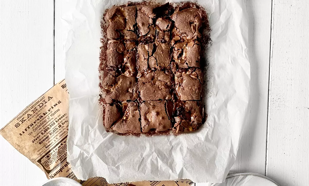 Hävikki-brownie on tumma, säröileväpintainen suorakaide, joka lepää vaalean leivinpaperin päällä puisella leikkuulaudalla