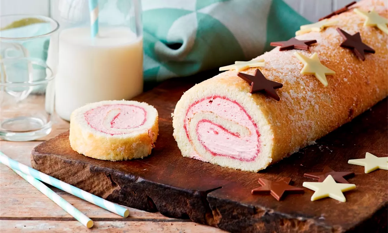 Vaaleanrapea kääretorttu, sisältä vaaleanpunainen kerma, päällystetty kevyellä tomusokerilla ja suklaatähdillä puunvärisellä tarjoilualustalla