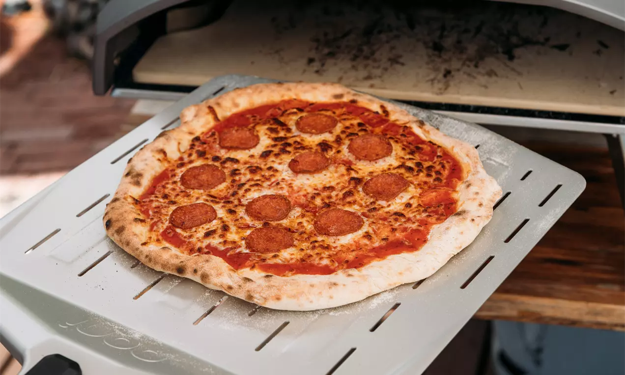 Kullanruskeareunainen pyöreä pizza, jolla sulanut juusto ja tummanpunaiset pepperoniviipaleet lepäävät ohuen tomaattikastikekerroksen päällä